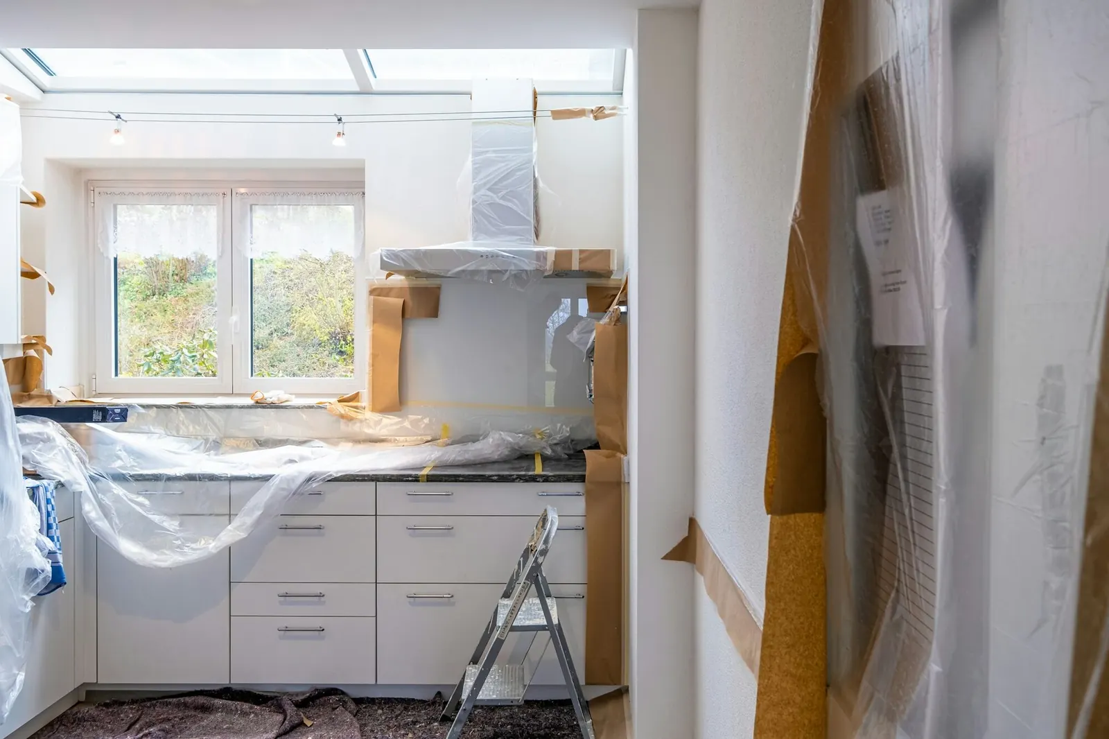 Kitchen mid-demolition with cabinets wrapped in plastic